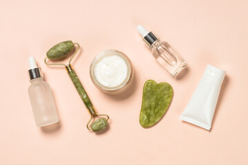 Cosmetic products - Jade roller and gua sha massager with cream and serum bottles. Spa background.