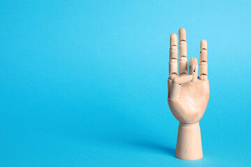 Wooden mannequin hand on light blue background. Space for text