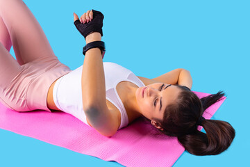 Young fitness pretty girl is lying on the fitness pink mat looking at the watch on her hand she...