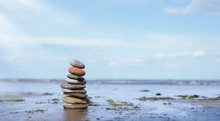 Fotobehang Zen Stenen Pebble tower by seaside with blurry seascape, Stack of Zen rock stones on the sand, Stones pyramid on the beach symbolizing, stability, harmony balance with shallow depth of field.  © Anchalee