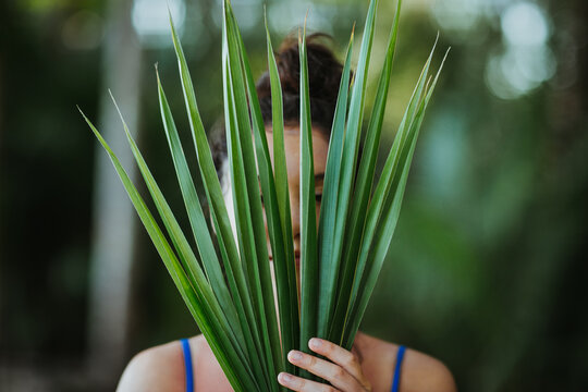 Woman covering face with palm tree leaves