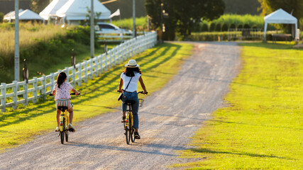 Family Happy.  Mother and daughter smiling happy outdoor with bicycling at the garden meadow in sunset.  Lifestyle Family Concept