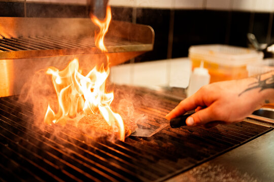 Crop cook grilling patty on grill in kitchen - Powered by Adobe