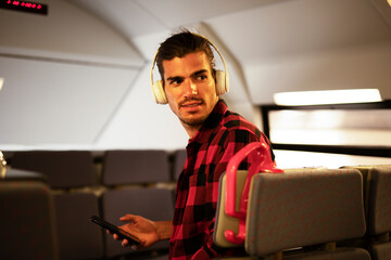 Young man listening to music while traveling by a train. Handsome young man traveling by a train...