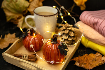 Obraz na płótnie Canvas Cocoa with milk in a white mug, pumpkins, garlands, a pine cone are on a tray. Autumn yellow leaves. Knitted sweater in a pile. Autumn season. Warm home atmosphere. Cozy home.