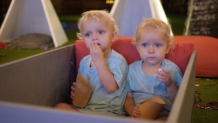 Two cute white twins watching movie with curiosity and eating kids popcorn