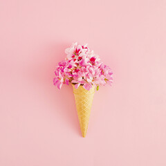 Creative idea of ice cream with .pink flowers in a cone on pink background. Minimal summer or dessert concept.