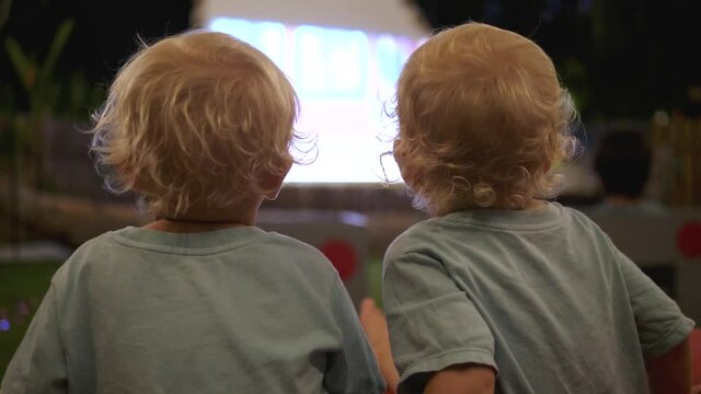 Back view of two blonde toddlers watching cartoon on a big screen