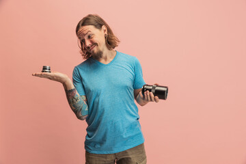 Fototapeta na wymiar Portrait of young man, photographer, cameraman with camera lens having fun isolated on pink studio background. Concept of occupation, job, funny meme emotions