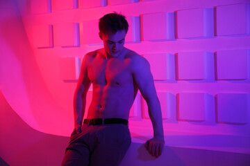 Young athletic guy with a naked torso in a neon red light.