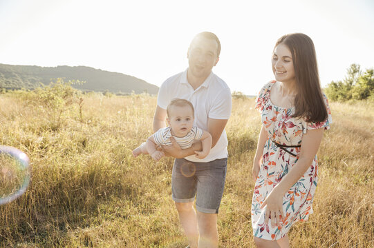 Happy young family with baby son playing and having fun together in nature on field