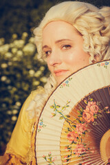 Portrait of blonde woman dressed in historical Baroque clothes with old fashion hairstyle, outdoors. Luxurious medieval dress