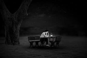 Fototapeta premium A black and white portrait of a young woman sitting on a chair lit by lanterns in the lonely night.