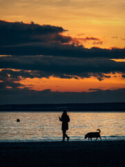 Silueta de una mujer paseando a su perro por la playa al atardecer