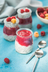 glass jars with chia pudding with raspberry and jam. Bowl of raspberry berry on the blue background.
