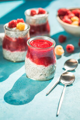 glass jars with chia pudding with raspberry and jam. Bowl of raspberry berry on the blue background.