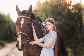 Obraz premium A beautiful young girl with long hair stands next to a horse in nature in the summer