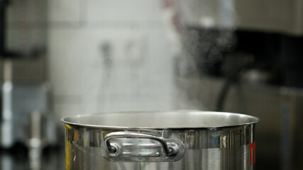 Vapour clouds rising from boiling water in pan on stove. Media. Steam and white smoke rising on professional kitchen background. Steam from pan while cooking. Cooking process in slow motion.