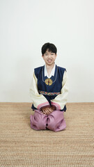 한복을 입고 미소지으며 멍석 위에 무릎 꿇고 앉아있는 소년 a boy kneeling...