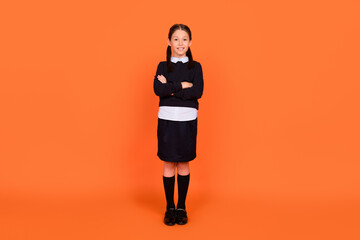 Full size photo of happy cheerful small girl hold hands folded confident lesson isolated on orange color background