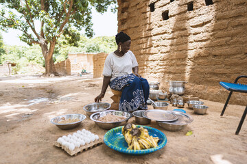Content young African housewife sitting in the middle of pots and pans in her rustic outdoor...
