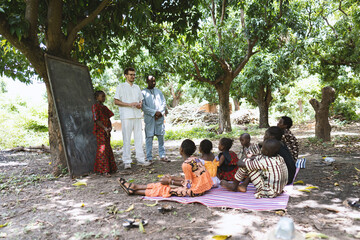 African teacher introducing a new white volunteer to a small group of destitute black schoolchildren in an open air classroom in a poor rural community center