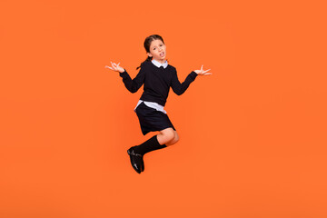Fototapeta na wymiar Full length photo of little brown braids haired girl jump shrug shoulders wear long socks uniform isolated on orange color background