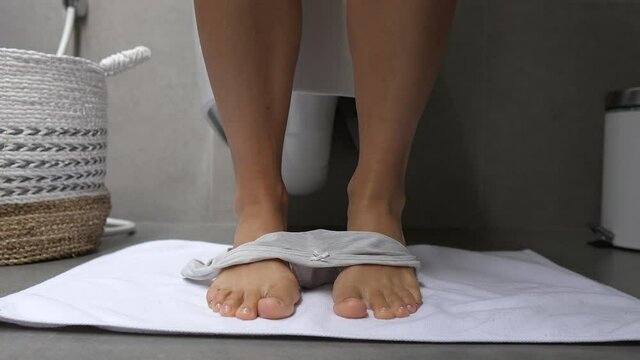 Close up of female legs of a woman in a toilet room taking off her underwear