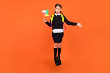 Fototapeta na wymiar Full length body size view of pretty funny schoolgirl jumping holding paper fan fooling isolated over bright orange color background