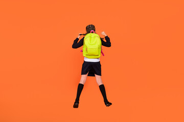 Fototapeta na wymiar Back rear spine view photo of small girl jump up wear backpack winner victory isolated on orange color background
