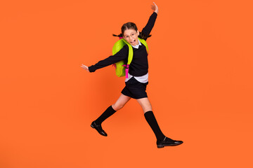 Full size photo of cheerful happy positive small girl jump up crazy wear bag isolated on orange...