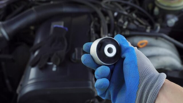 master in glove holds lever silent block in his hand against background of engine. rubber metal hinge, elastic part is connected to internal and external connections by vulcanization. car service.