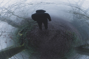 A hooded figure, back to camera, on a woodland path. On a foggy, spooky, winters day. With an...