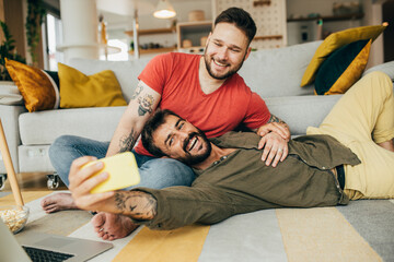 Young happy gay couple sitting and lying on the floor and posing for a good photo. They are taking selfies.