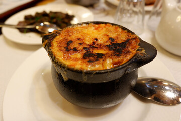 Burned cheese crust on the pot with French traditional onion soup in restaurant in Pau, France