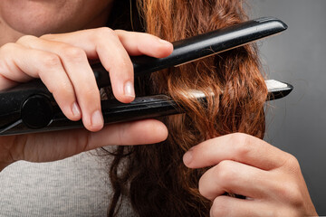 girl straightens curly hair with an iron.
