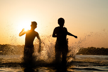 Happy kids running and splashing in the sea at sunset. Summer vacation and healthy lifestyle concept