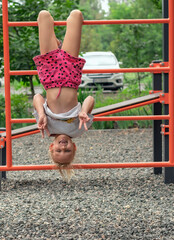 girl 6-7 years old is playing cheerfully on the playground, hanging upside down