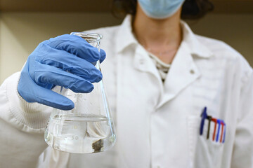 Young female scientist holding erlenmeyer flask, select focus