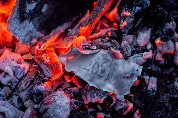 Burnt paper with still readable inscription 2021 in the fire. Concept of unsuccessful 2021 year,...
