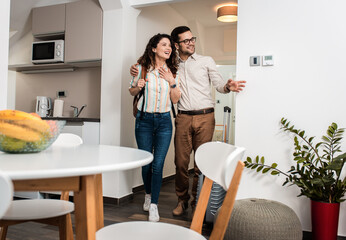 Smiling couple with suitcase arriving in apartment.