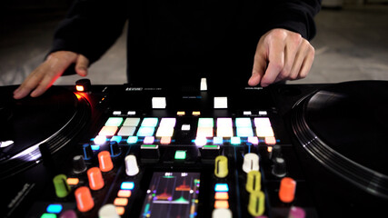 Close up of DJ using a modern sound mixer for playing electro music at the nightclub. Art. Colorful Buttons and vinyl, equipment of a deejay.