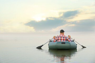 Man rowing inflatable rubber fishing boat on river, back view. Space for text