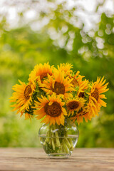 glass vase with a bouquet of beautiful yellow sunflower flowers on an old rustic wooden table in the garden