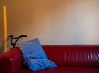 Dim light living room scene with blue pillow slouching on red sofa, with small BMX hidden behind