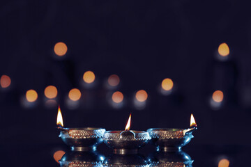 Lit diyas on table against blurred lights. Diwali lamps