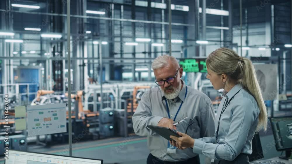 Leinwandbilder Car Factory Office: Scientist Talks with Senior Engineer, Use Tablet Computer to Design Production Conveyor for Advanced Power Engines. Automated Robot Arm Assembly Line Manufacturing Vehicles