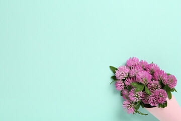 Bouquet of beautiful clover flowers on turquoise background, top view. Space for text