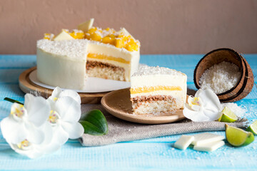 Festive coconut cake. White cake with mango for a party. Pieces of white chocolate. A piece of cake on a plate. Birthday. Delicious tropical dessert. Orchids on a blue background
