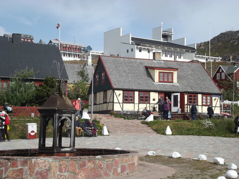 Fountain and historic houses on the market square of Qaqortog, Iceland, in the background the modern Gertrud Rask Church